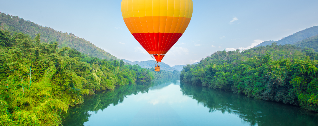 Bild eines Heißluftballons über einem Fluß, der von dichtem, grünen Buschwerk umrahmt ist