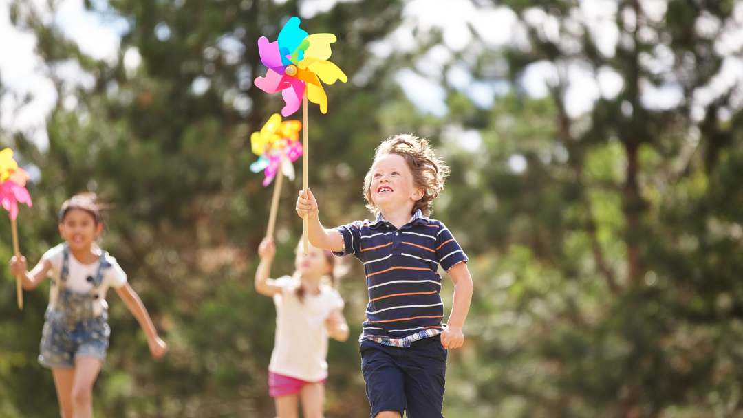 Kinder laufen mit Spielzeug-Windrädern über eine Wiese